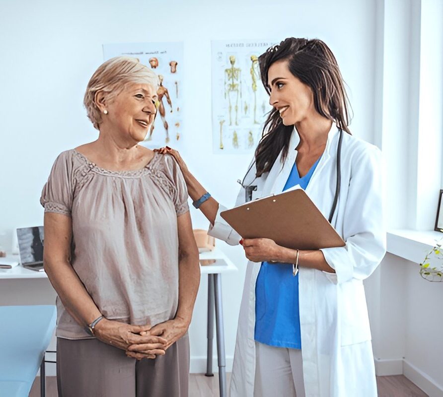 Alternative Text (Alt Text): Female doctor with clipboard smiling and speaking to an elderly female patient during a senior healthcare consultation.