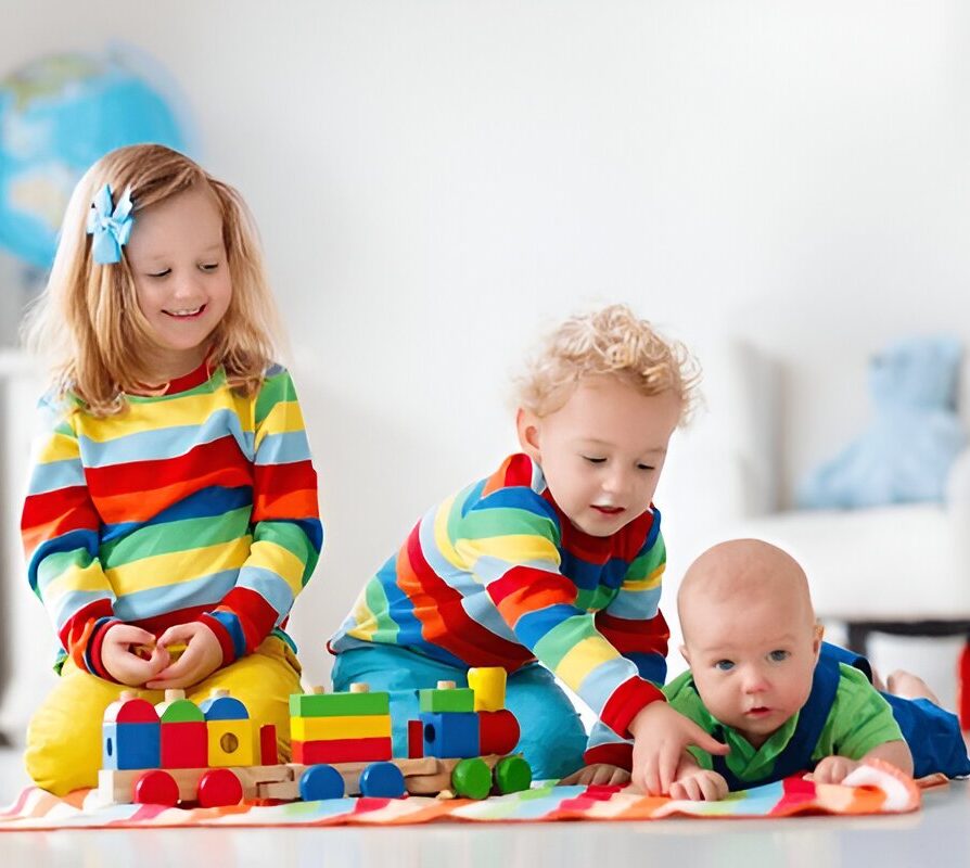 Three young children playing with colorful wooden toys on the floor in a bright daycare setting.